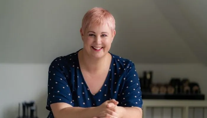 Judith Huinink in haar praktijk in Arnhem, lachend aan tafel met natuurlijke verzorgingsproducten op de achtergrond